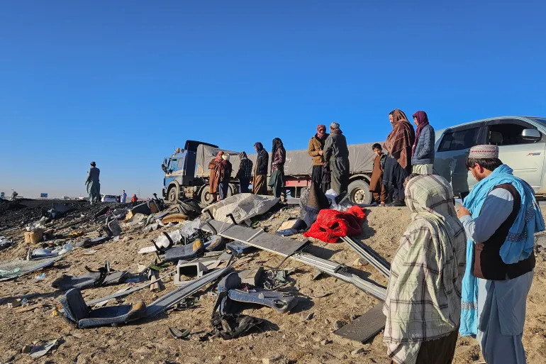 Afghan residents inspect the accident site as they stand near the remains of a bus following its collision with a coal truck on a highway between Kabul and southern Kandahar city [Mohammad Faisal Naweed/AFP]